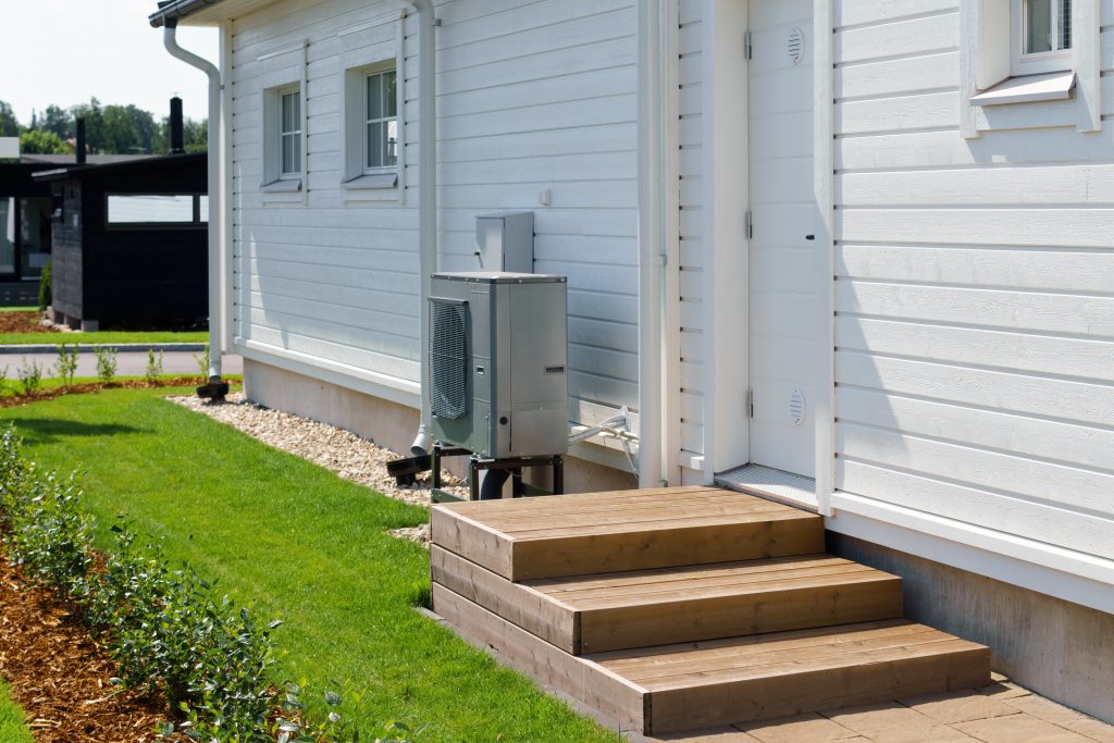 Air source heat pump installed on the exterior of a modern wooden house. Air source heat pump reduces heating costs and your home's carbon footprint.