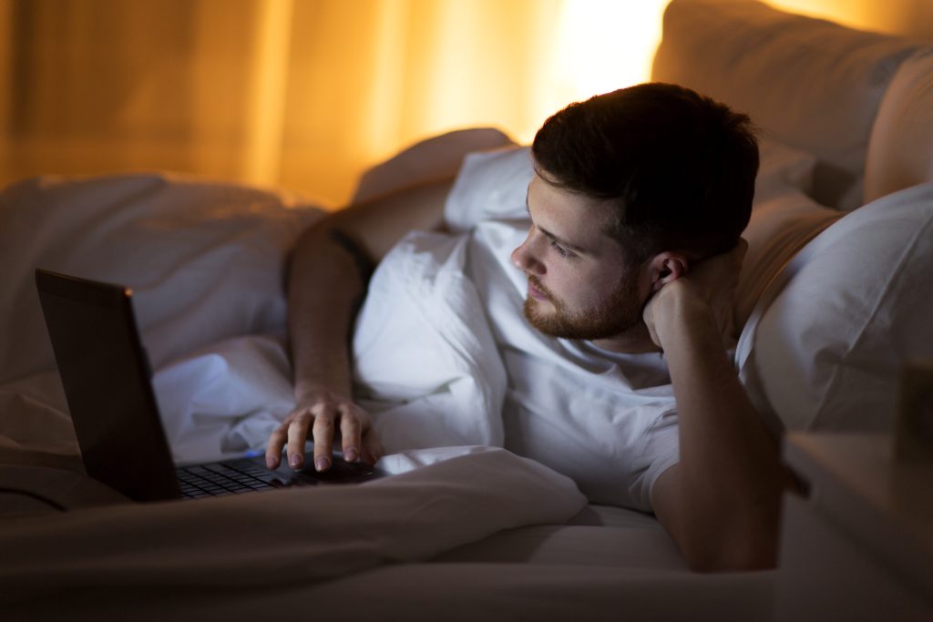 a man using a laptop in bed 