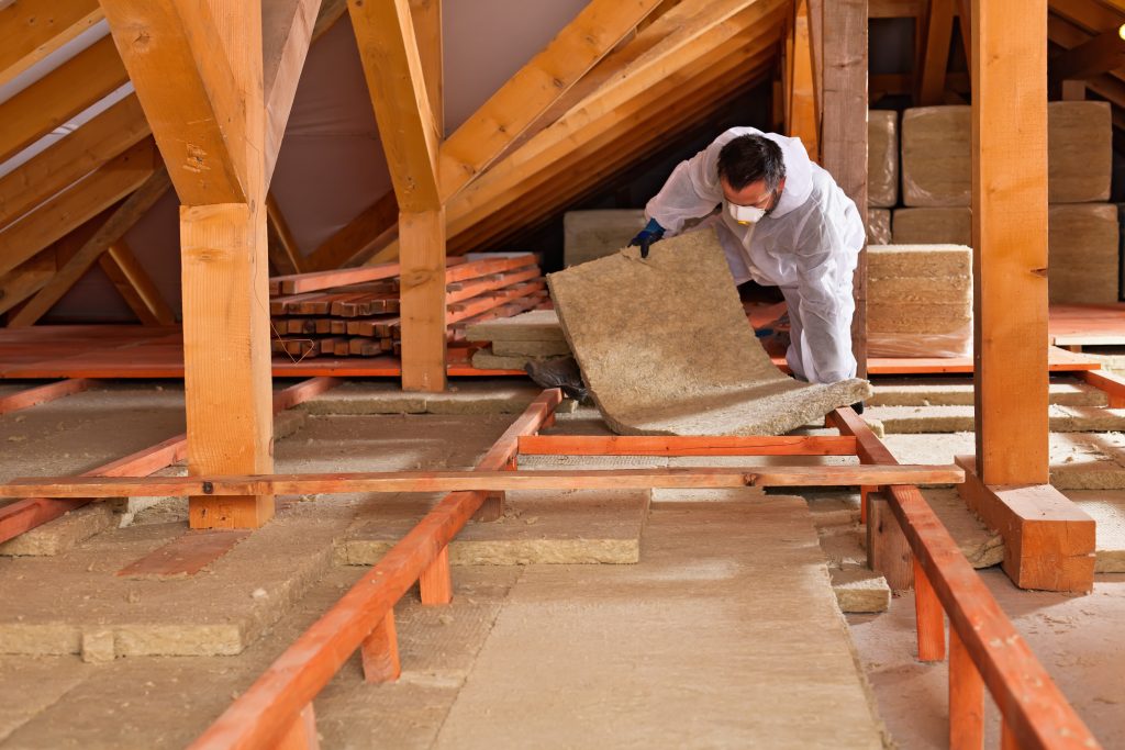a man installing loft insulation in a large loft wearing PPE