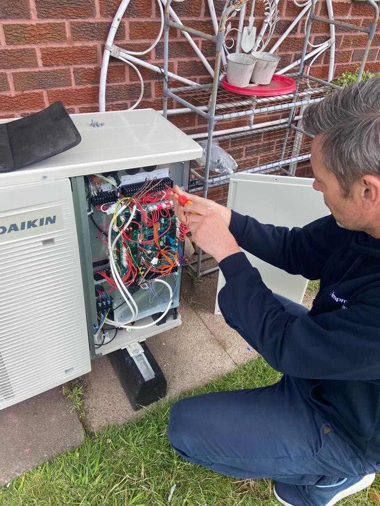 an installer examining the internal wiring of an air source heat pump