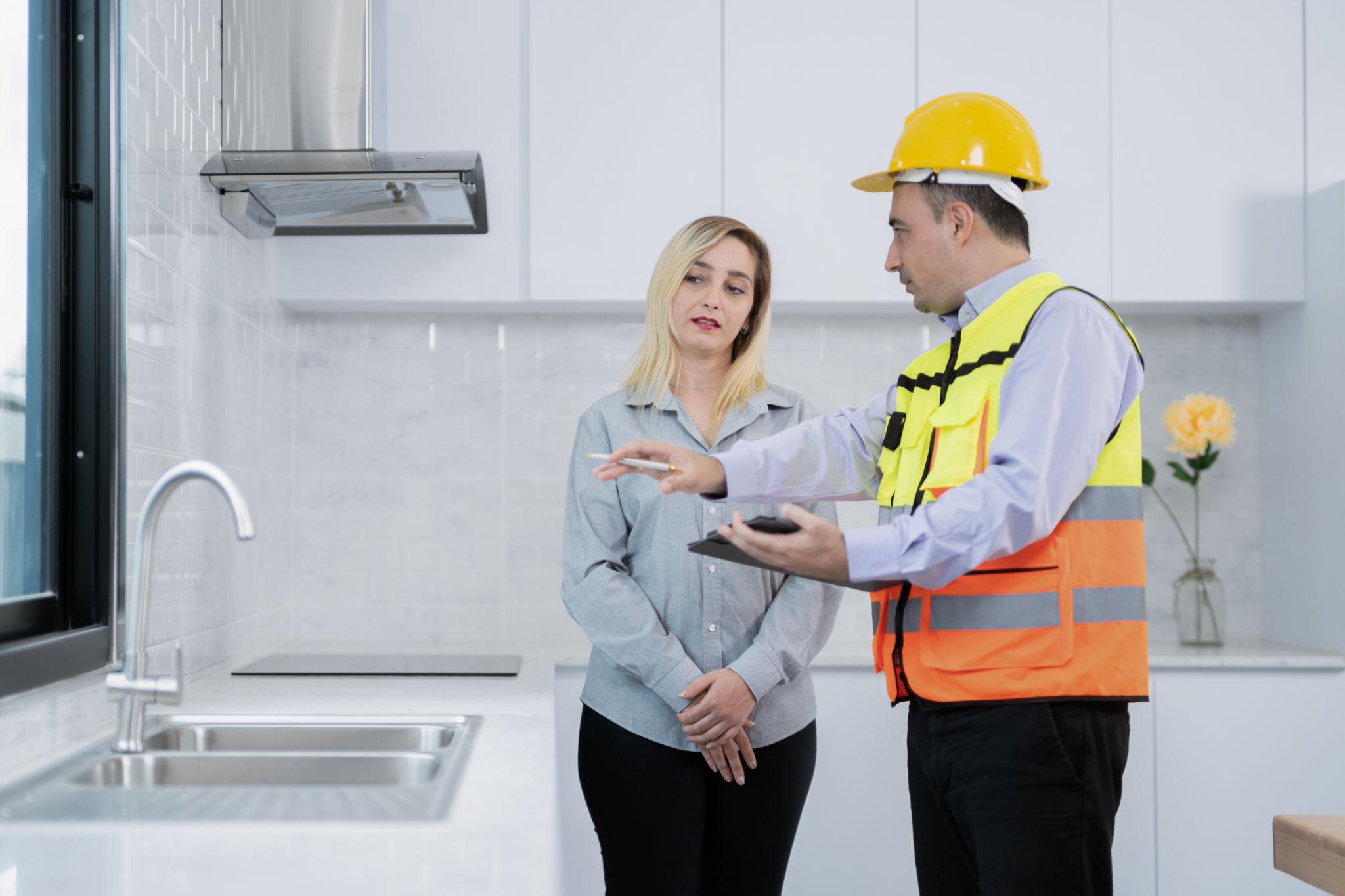Installer explaining home survey details to a homeowner in a kitchen during a property assessment