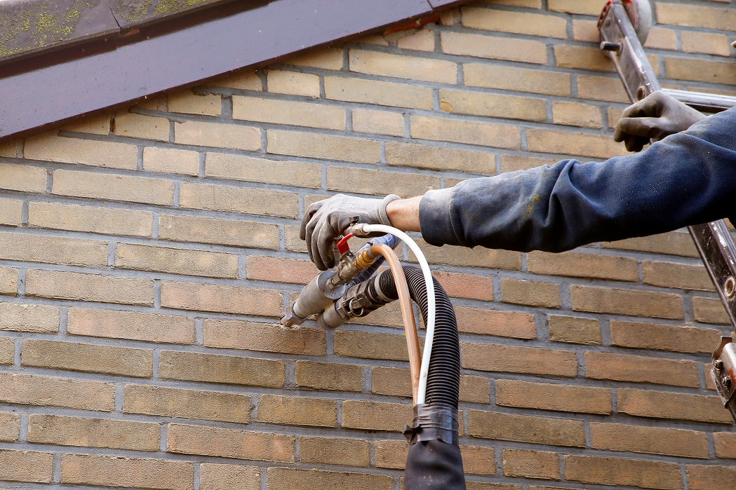 Technician injecting cavity wall insulation into a brick exterior wall using specialist equipment