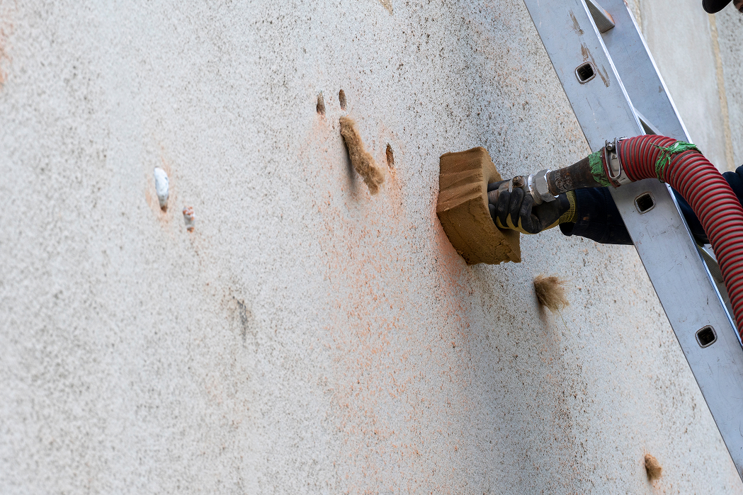 Worker drilling holes into external wall to prepare for insulation installation